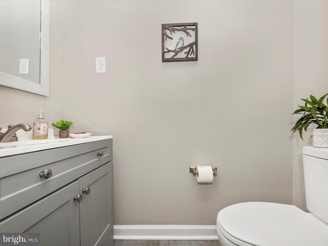 half bathroom with toilet, vanity, and baseboards