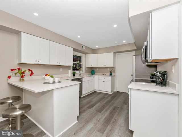 kitchen with a kitchen bar, a peninsula, white cabinets, light countertops, and light wood-style floors