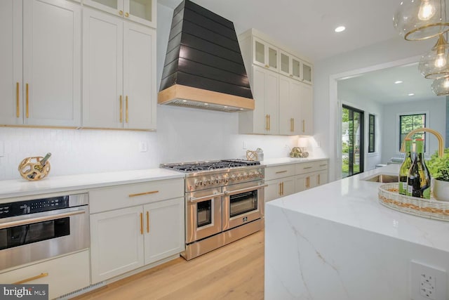 kitchen featuring stainless steel appliances, custom exhaust hood, light wood-style flooring, white cabinetry, and recessed lighting