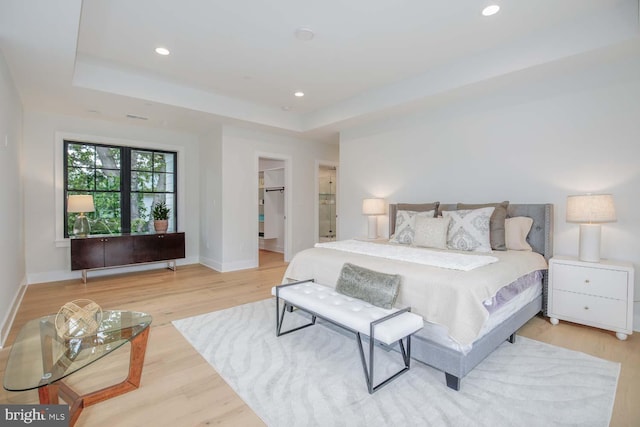 bedroom with a tray ceiling, light wood-style floors, baseboards, recessed lighting, and a walk in closet
