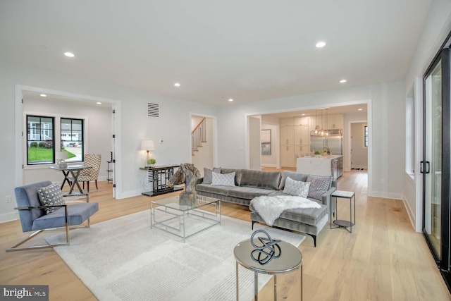 living room with stairs, healthy amount of natural light, light wood finished floors, recessed lighting, and baseboards