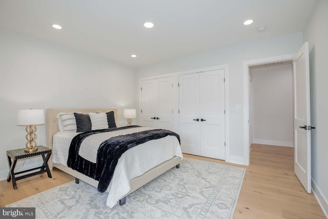 bedroom featuring two closets, light wood finished floors, baseboards, and recessed lighting
