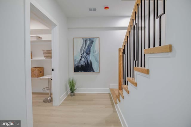corridor featuring light wood-type flooring, stairs, and baseboards
