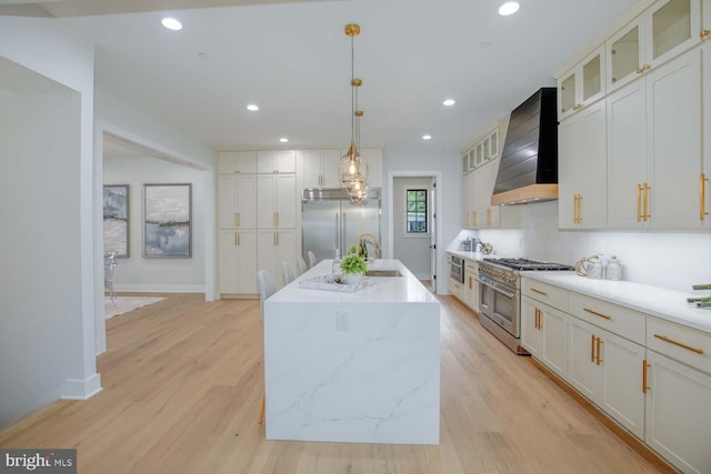 kitchen with premium appliances, wall chimney range hood, a sink, light wood-type flooring, and recessed lighting