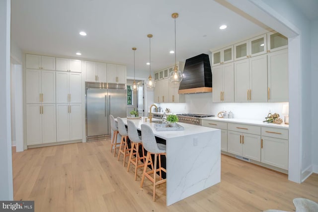 kitchen with custom range hood, appliances with stainless steel finishes, a kitchen breakfast bar, light wood-type flooring, and recessed lighting