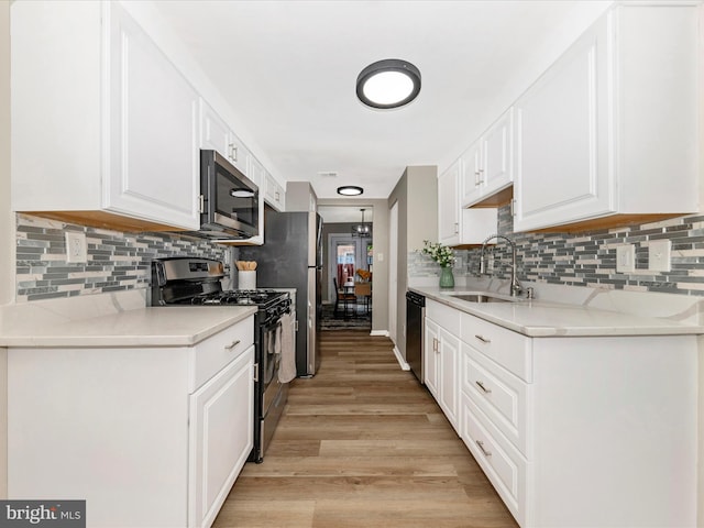 kitchen featuring appliances with stainless steel finishes, a sink, light wood-style floors, white cabinetry, and backsplash
