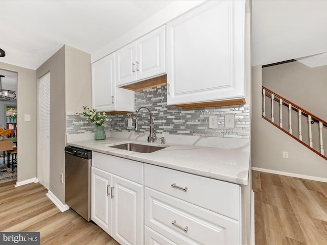 kitchen featuring stainless steel dishwasher, a sink, light wood-style flooring, and backsplash