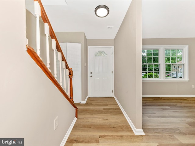 foyer entrance featuring light wood-style floors, stairway, and baseboards