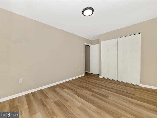 unfurnished bedroom featuring light wood-type flooring, baseboards, and a closet