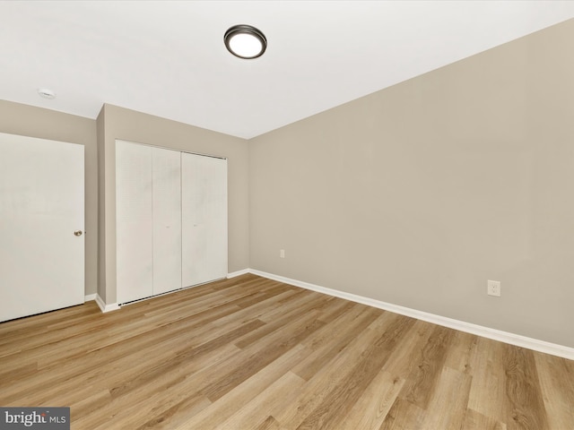unfurnished bedroom featuring light wood-style flooring, a closet, and baseboards