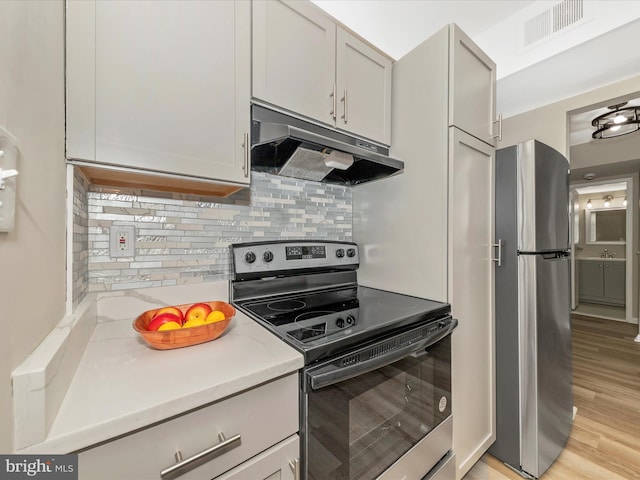 6994 Hanover Pkwy Unit 101, Greenbelt, MD 20770 - kitchen with stainless steel appliances, under cabinet range hood, light countertops, backsplash, and light wood-type flooring