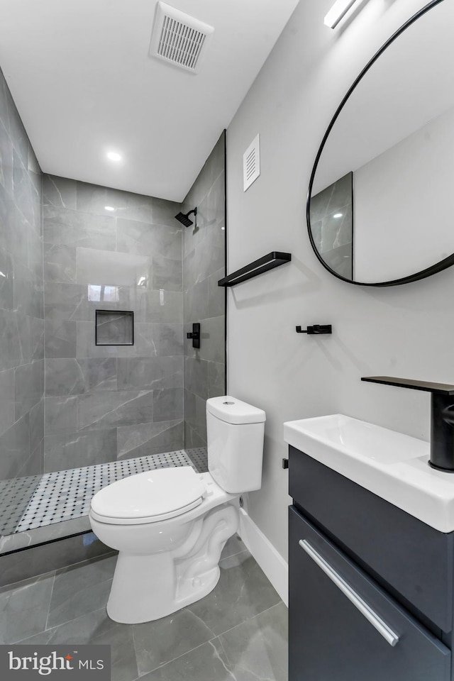 full bath with toilet, tiled shower, vanity, and baseboards