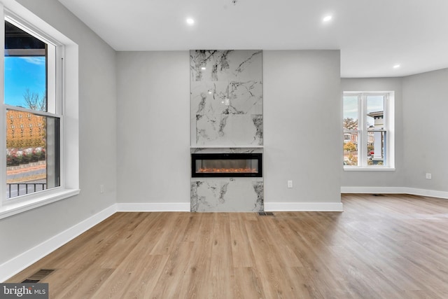 unfurnished living room with recessed lighting, a premium fireplace, wood finished floors, and baseboards