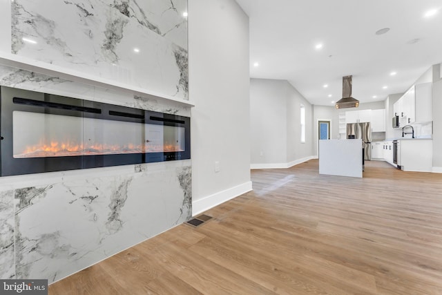 kitchen with stainless steel refrigerator with ice dispenser, island range hood, white cabinetry, light wood-style floors, and recessed lighting