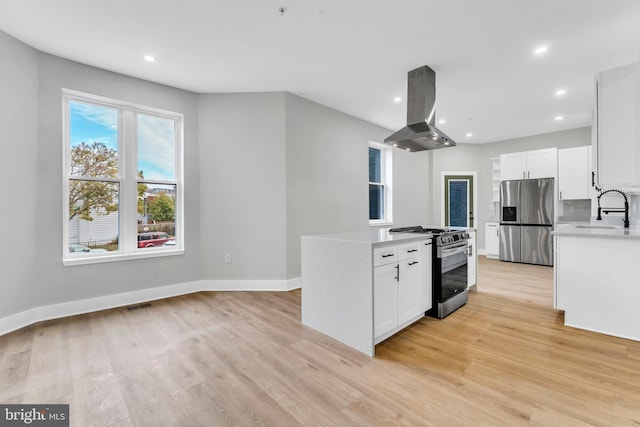 kitchen with appliances with stainless steel finishes, island exhaust hood, light countertops, light wood-style floors, and a sink