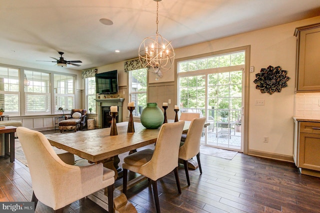 dining area featuring dark wood-style floors, a chandelier, a fireplace, ceiling fan, and baseboards