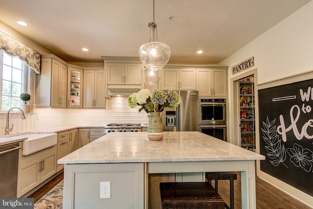 kitchen featuring a sink, appliances with stainless steel finishes, dark wood finished floors, light stone counters, and decorative backsplash