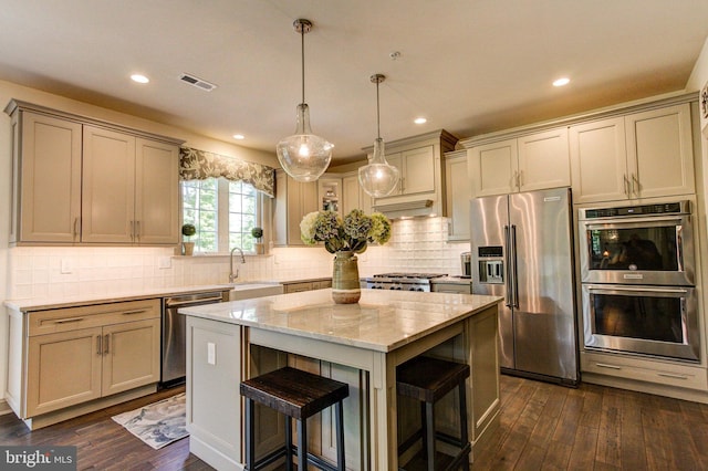 kitchen with appliances with stainless steel finishes, a sink, a kitchen island, dark wood-type flooring, and light stone counters