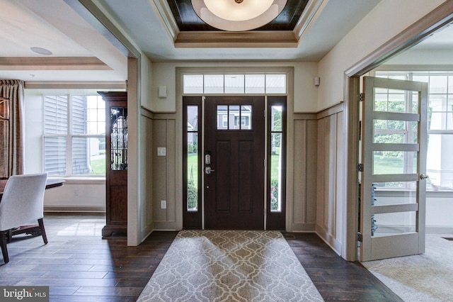 foyer entrance featuring a raised ceiling, dark wood-style flooring, a decorative wall, and crown molding