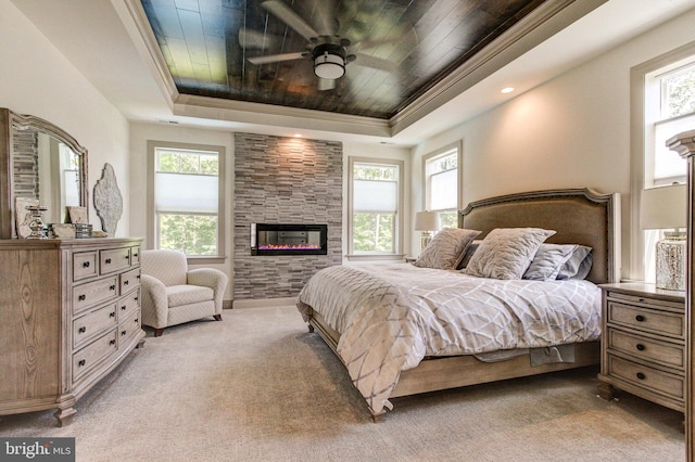 bedroom featuring a tray ceiling, multiple windows, light carpet, wood ceiling, and a large fireplace