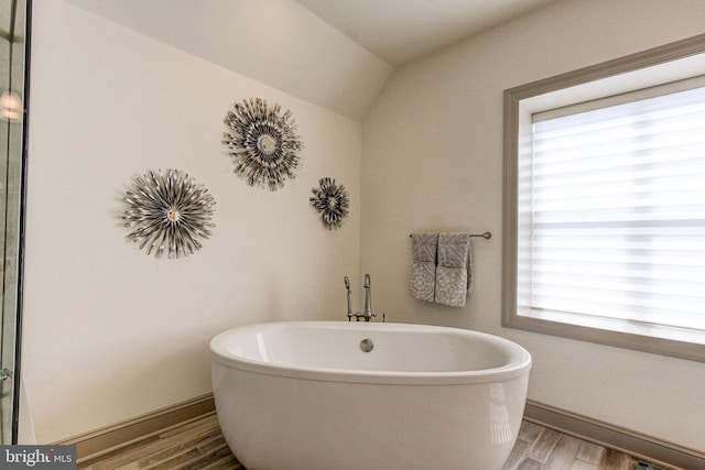 bathroom with wood finished floors, a freestanding bath, baseboards, and vaulted ceiling