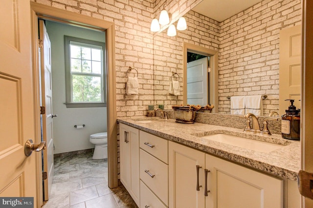 bathroom featuring toilet, double vanity, brick wall, and marble finish floors