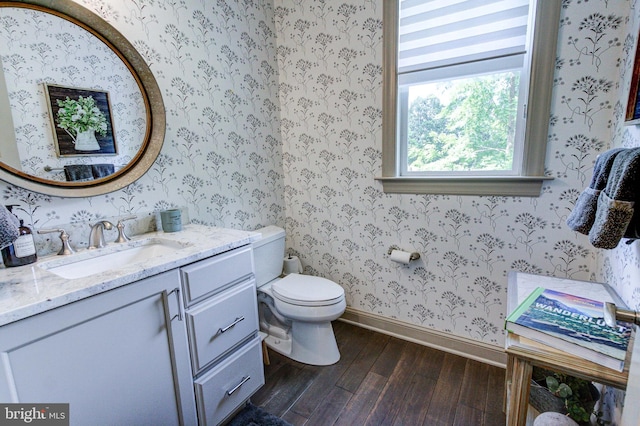 half bath featuring wood finished floors, baseboards, toilet, vanity, and wallpapered walls