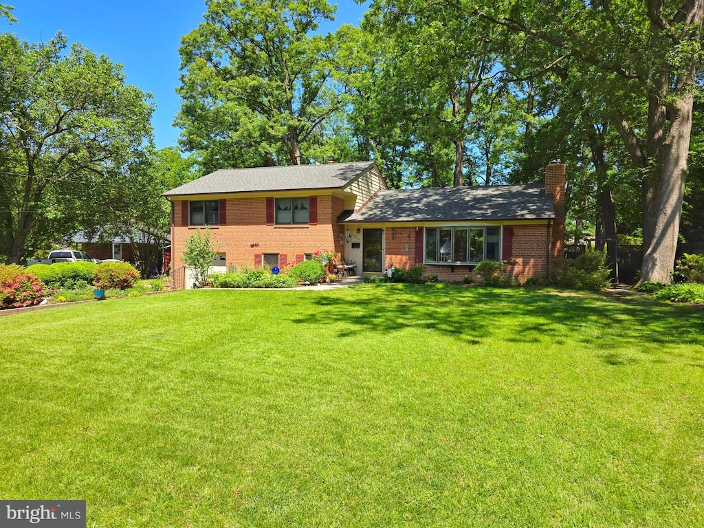 tri-level home featuring a front yard, brick siding, and a chimney