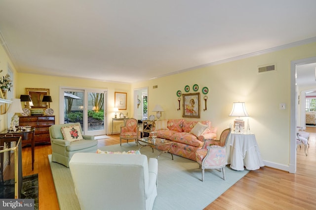 living area featuring ornamental molding, light wood-type flooring, and baseboards