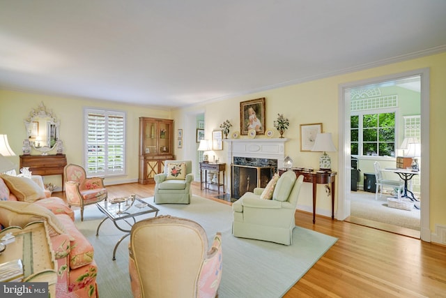 living area with plenty of natural light, a premium fireplace, light wood-style flooring, crown molding, and baseboards