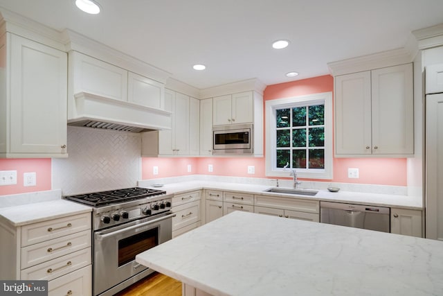 kitchen with appliances with stainless steel finishes, a sink, light stone counters, backsplash, and white cabinets