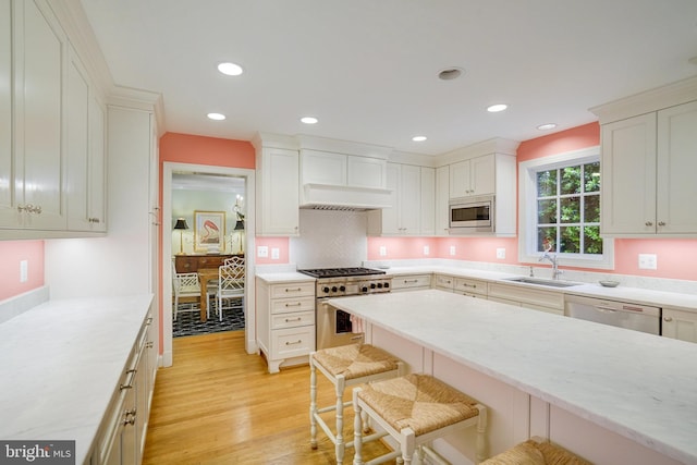 kitchen with stainless steel appliances, a breakfast bar, light wood finished floors, a sink, and custom range hood