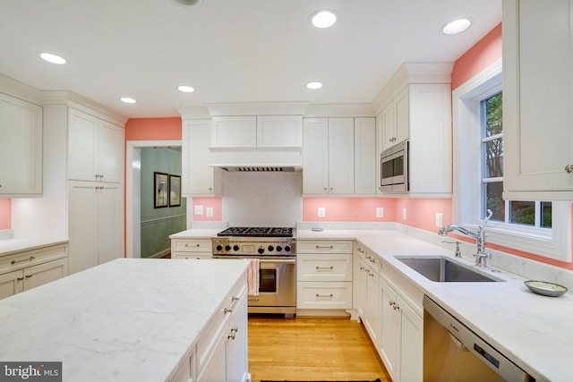 kitchen featuring stainless steel appliances, a sink, light stone counters, white cabinets, and recessed lighting