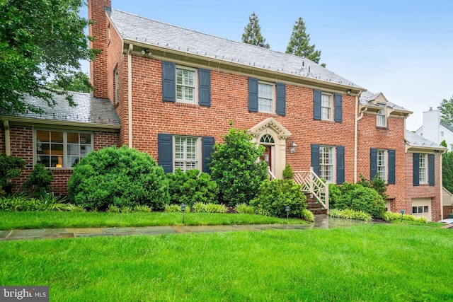 colonial inspired home featuring a chimney, a front lawn, brick siding, and a high end roof