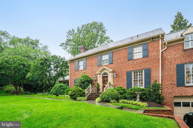 view of front of home featuring a chimney, a front yard, brick siding, and an attached garage