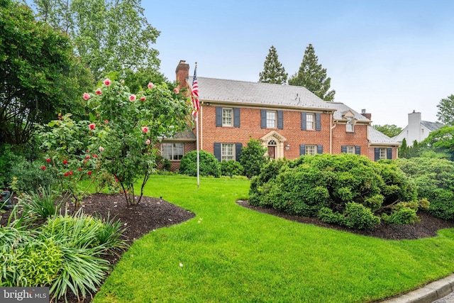 view of front of property with a chimney, brick siding, and a front yard