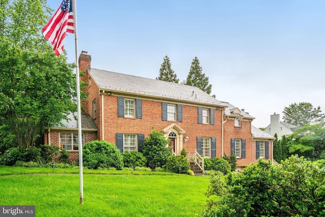 view of front of house with a chimney, brick siding, and a front yard