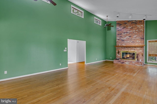 109 Kingfisher Cir, Weems, VA 22576 - unfurnished living room with ceiling fan, track lighting, wood finished floors, a brick fireplace, and a towering ceiling