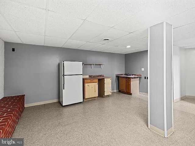 kitchen featuring freestanding refrigerator, baseboards, and a drop ceiling