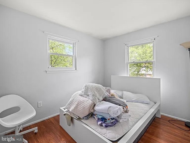bedroom with multiple windows, wood finished floors, and baseboards