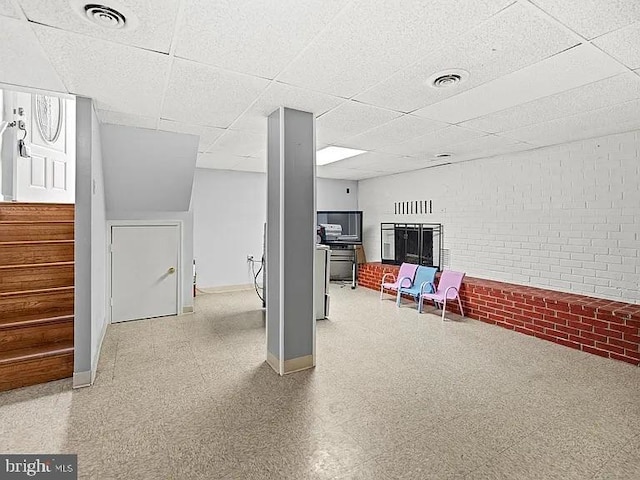 basement featuring baseboards, tile patterned floors, a drop ceiling, brick wall, and stairway