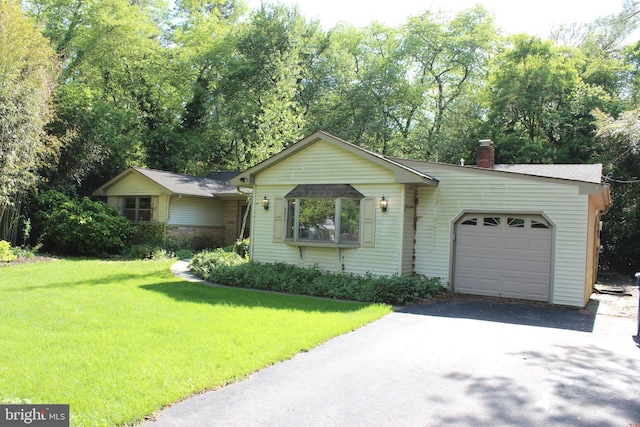 view of front of property with a garage, asphalt driveway, a front yard, a chimney, and view of wooded area