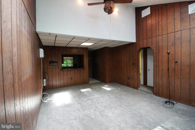 unfurnished living room with carpet, ceiling fan, wood walls, and arched walkways