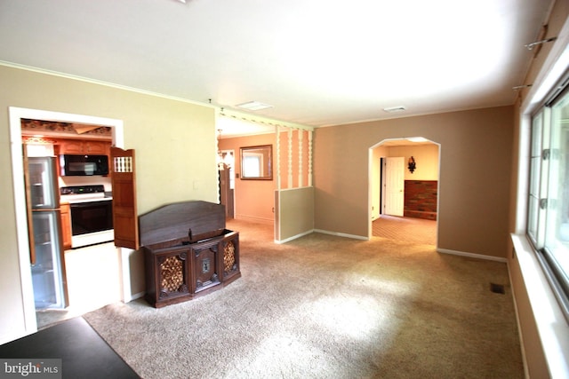 empty room with arched walkways, light colored carpet, ornamental molding, baseboards, and healthy amount of natural light
