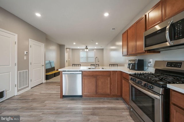 45 Quigley Ct, Camden Wyoming, DE 19934 - kitchen with stainless steel appliances, a peninsula, brown cabinetry, a sink, and light wood-type flooring