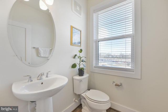 half bath with plenty of natural light, baseboards, toilet, and a sink