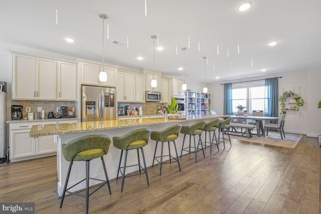 kitchen with stainless steel appliances, a large island with sink, a kitchen bar, dark wood-type flooring, and decorative backsplash