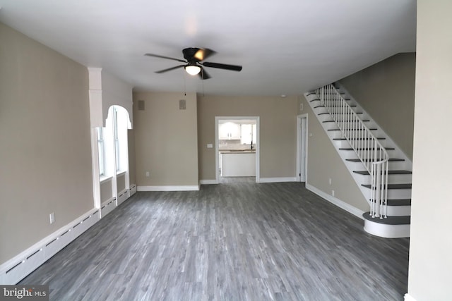 unfurnished living room featuring a ceiling fan, wood finished floors, stairs, and baseboards
