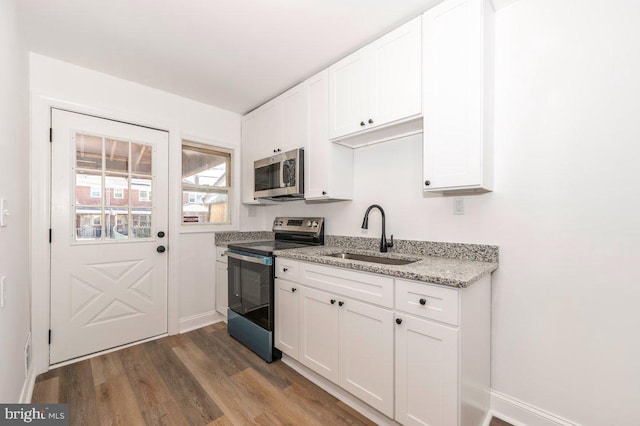 kitchen with appliances with stainless steel finishes, a sink, white cabinets, and dark wood-type flooring