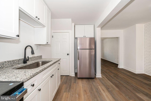 kitchen featuring freestanding refrigerator, a sink, white cabinets, dark wood finished floors, and light stone counters